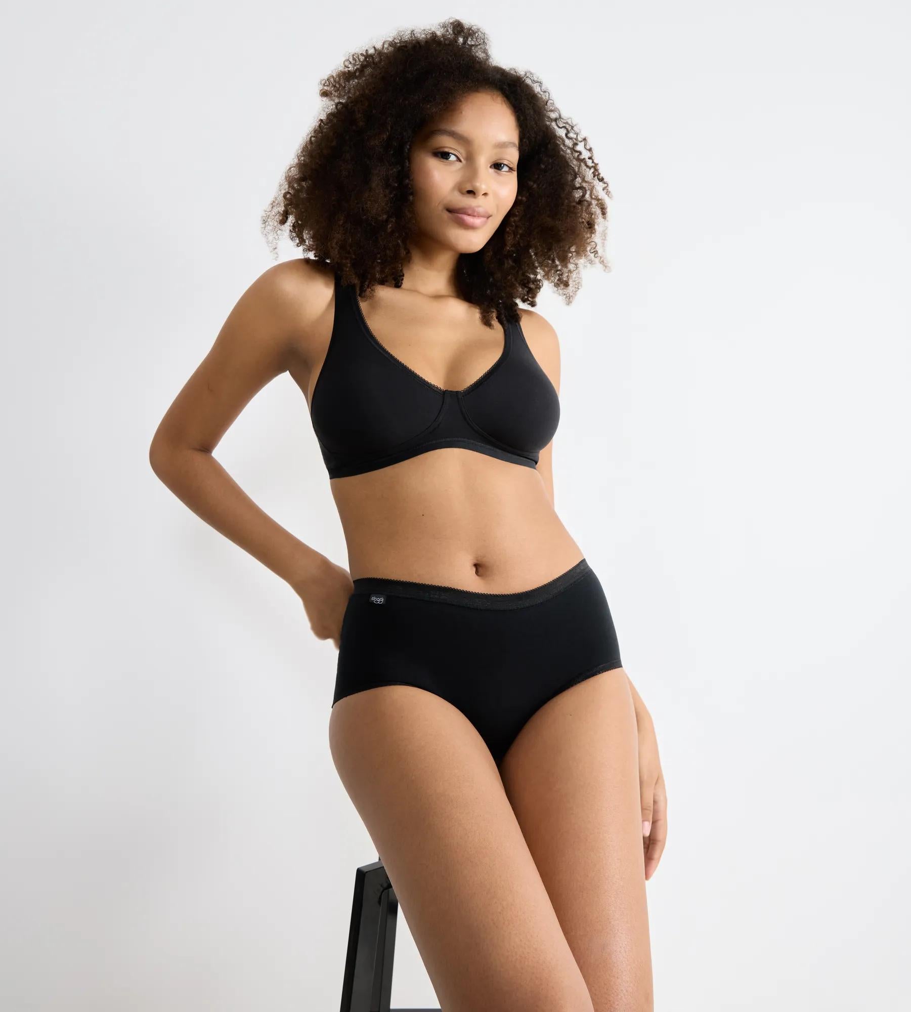 Woman wearing sloggi Basic+ 4-pack black bra and briefs, showcasing comfort and style.