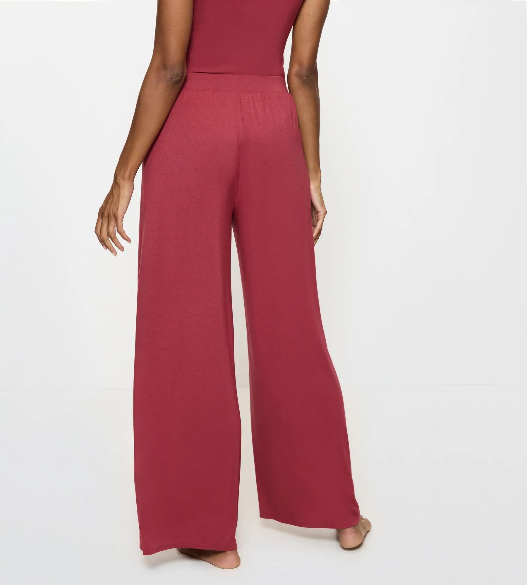 Model wearing back view of Aura Spotlight wide leg trousers in burgundy, showcasing comfort and style.